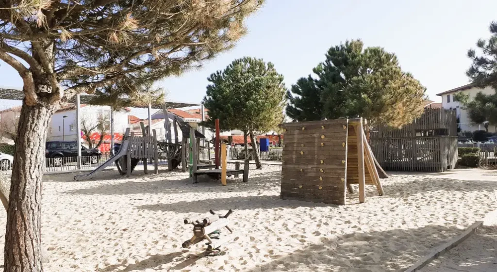jeux-enfants-centre Une aire de jeux en bois pour enfants dans un bac à sable entouré de végétation